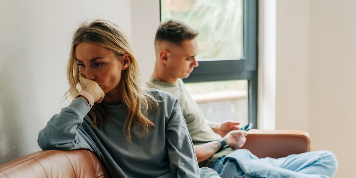 Woman looking upset, man in background on his phone