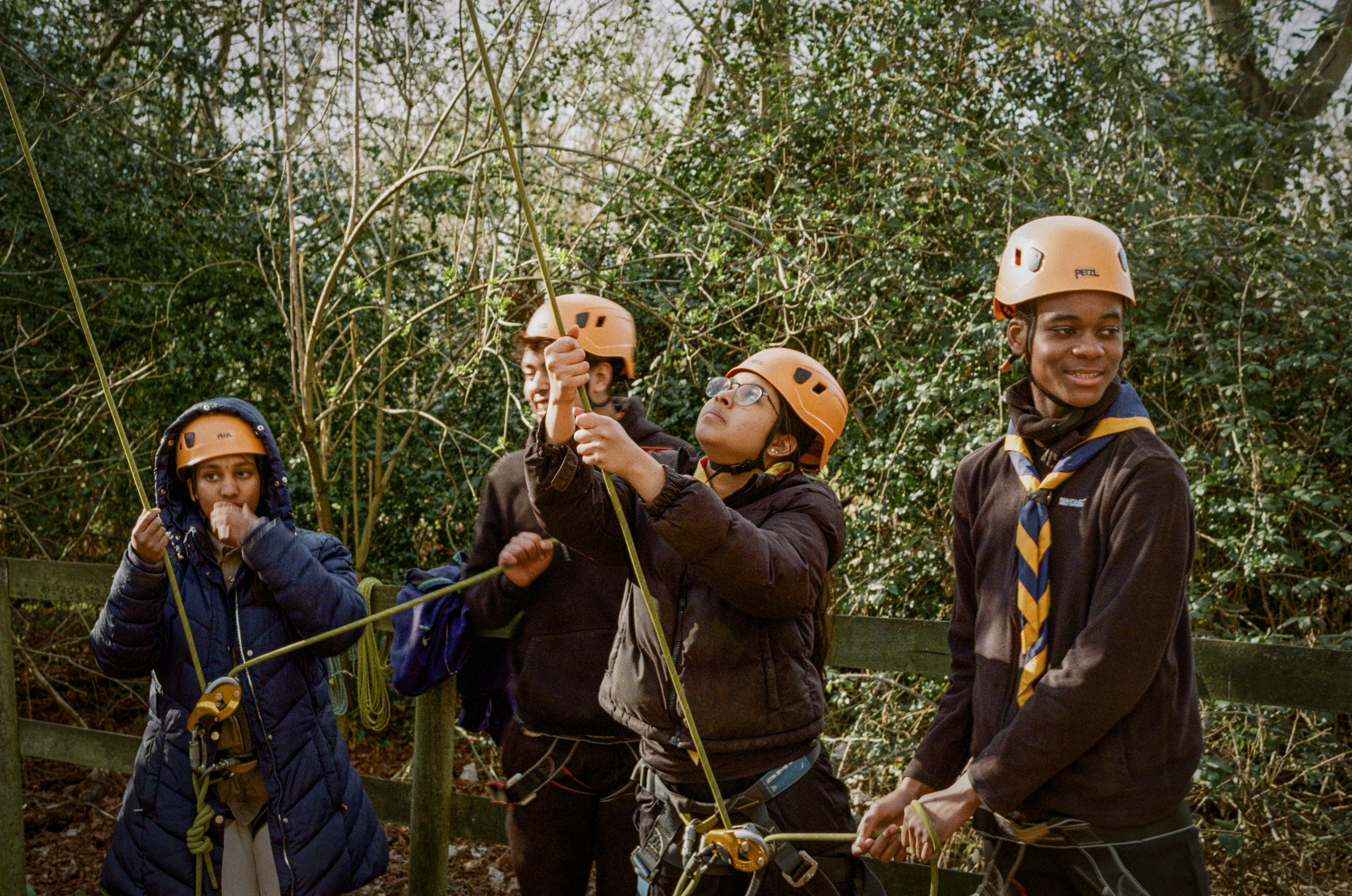 Image shows four Scouts in neckers and helmets doing a rope activity