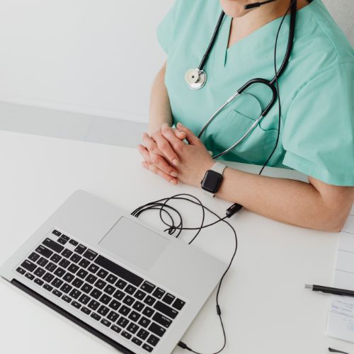 A healthcare professional in blue scrubs sat next to a laptop