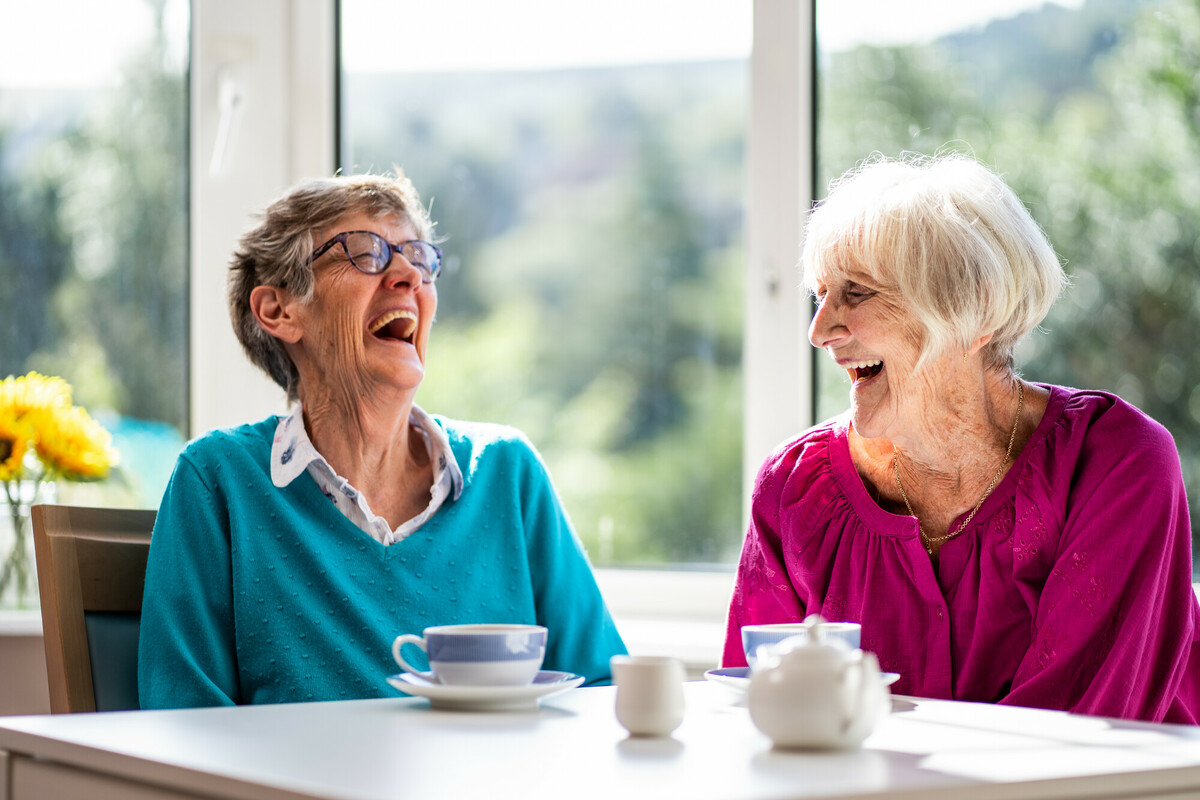 Two older women sat in front of a window laughing