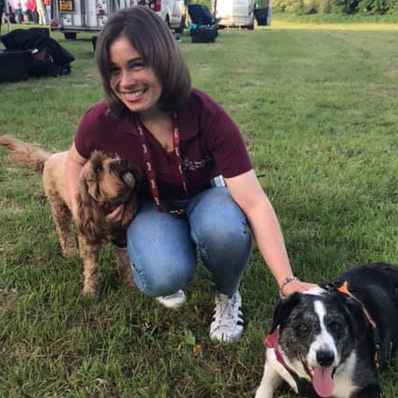 Rachel Annetts wearing a Hearing Dog uniform with two dogs by her side. Rachel Annetts wearing a Hearing Dog uniform with two dogs by her side.