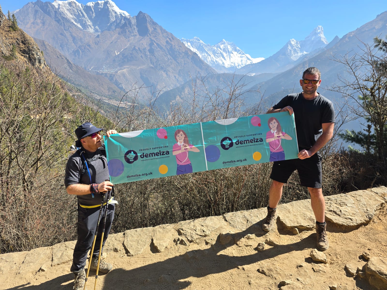 Two people climbing Everest hold a Demelza banner